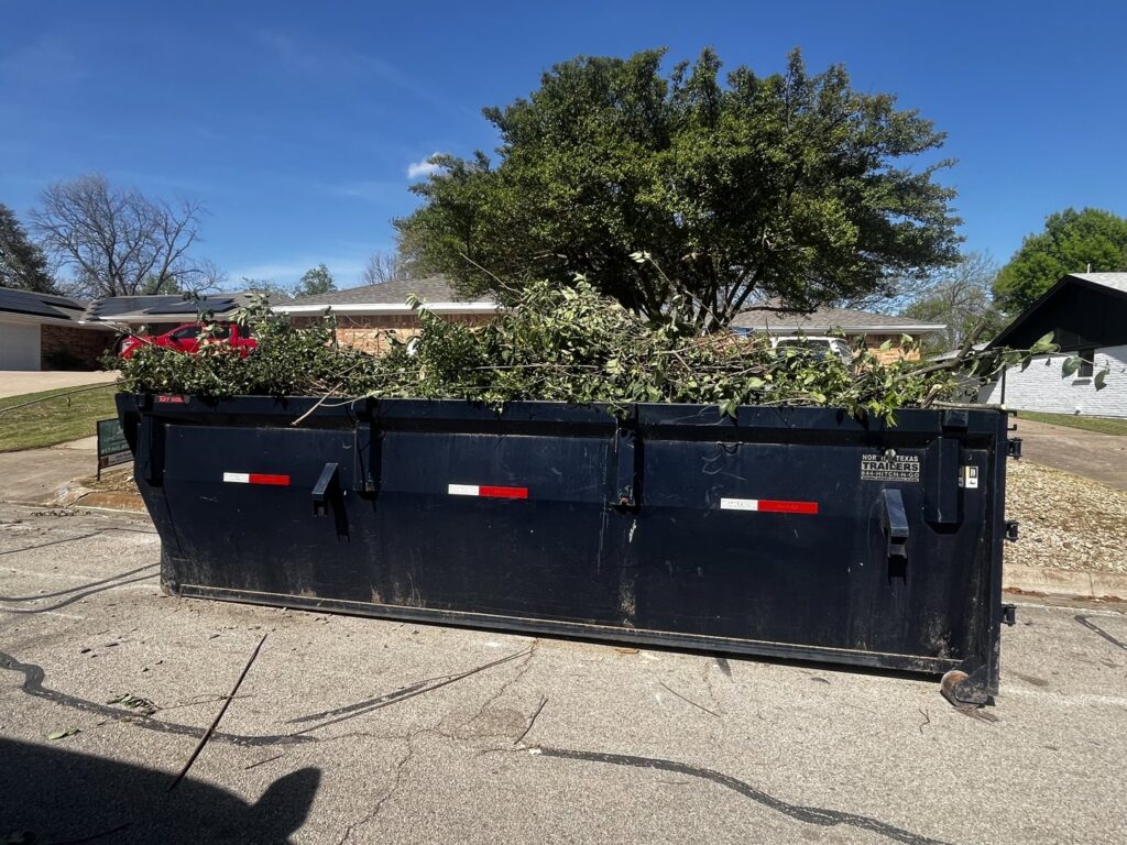 A large dumpster filled with tree branches and yard waste, ready for removal by Cowtown Waste Removal in Fort Worth, TX.