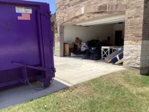 A purple dumpster from Liberty Hill Dumpster Rental positioned for a garage cleanout with junk visible in Austin, TX