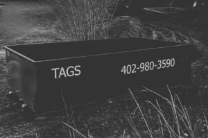A black Tags Dumpsters roll-off dumpster placed in a grassy area, ready for debris collection in Omaha, NE.