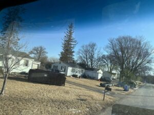 A large black dumpster placed on a grassy slope near residential homes by NID Dumpster Rental in Nashua, IA.