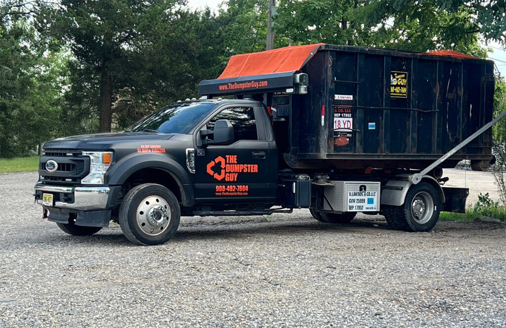 A branded junk removal truck from The Dumpster Guy, equipped with a roll-off container in Webster, MA.