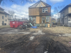 A red roll-off dumpster from The Dump Town next to a house with renovation debris in Detroit, MI.