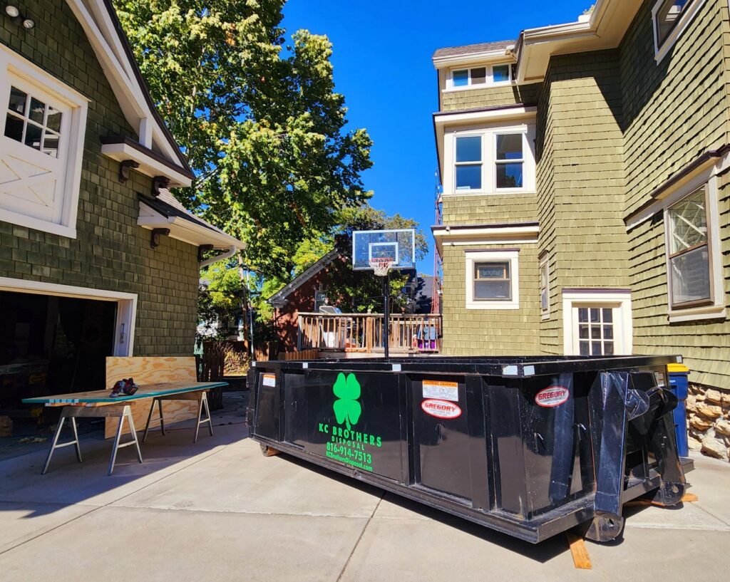 A KC Brothers Disposal dumpster parked next to a house undergoing renovation in Kansas City, MO, for debris removal.