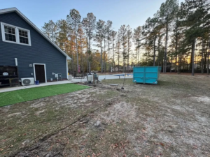 A blue dumpster placed in a residential backyard for a cleanup project by Site Boss Dumpster Rentals in Raeford, NC.