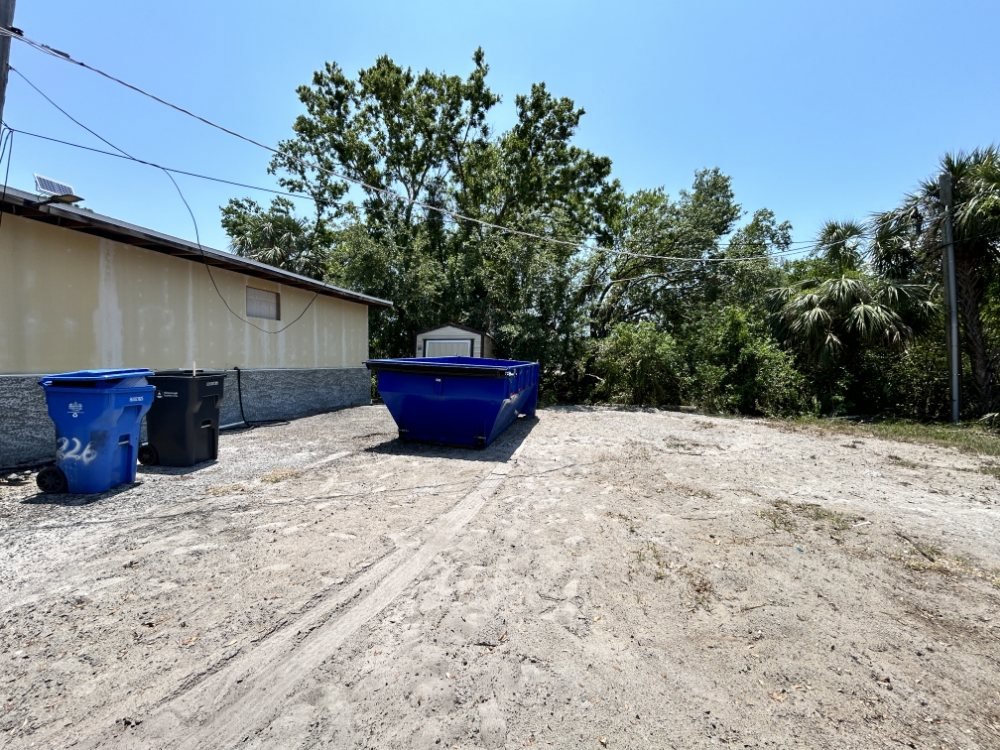 An empty blue dumpster placed in a dirt area for general junk removal by R&Y Dumpster Kings in Tampa, FL.