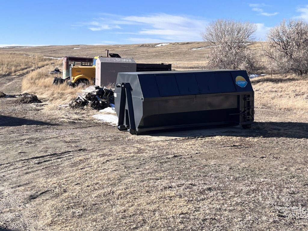 A roll-off dumpster placed in a field next to old equipment, ready for junk removal by First Light Services Llc in Casper, WY.