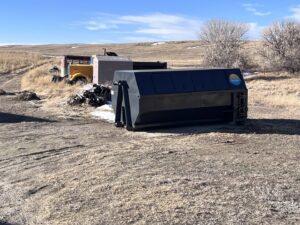 A roll-off dumpster placed in a field next to old equipment, ready for junk removal by First Light Services Llc in Casper, WY.