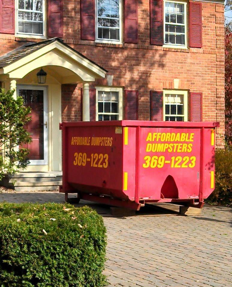 A red dumpster from Affordable Dumpsters placed in front of a brick house for junk removal in Watervliet, NY.