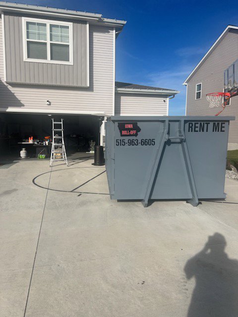 A grey roll-off dumpster placed in a residential driveway in front of a garage by Iowa Roll Off in Ankeny, IA.