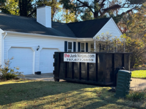 A black dumpster from The Junk Ninjas placed in a residential driveway in front of a garage in Hampton Roads, VA.