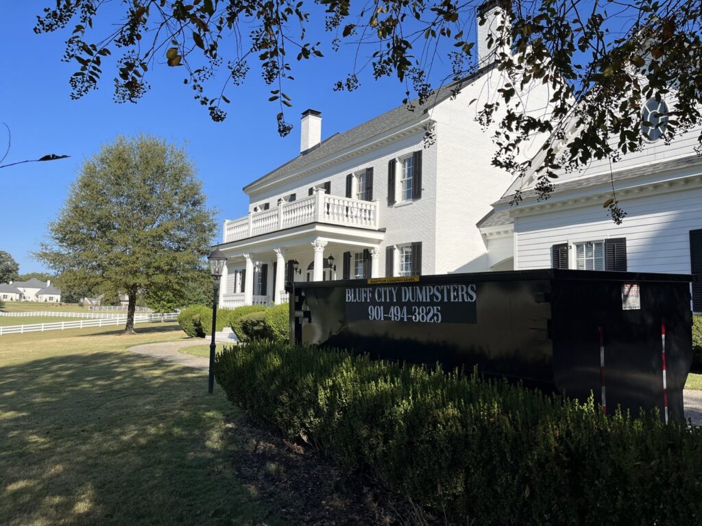 A Bluff City Dumpsters roll-off dumpster positioned in front of a large white house in Memphis, TN.