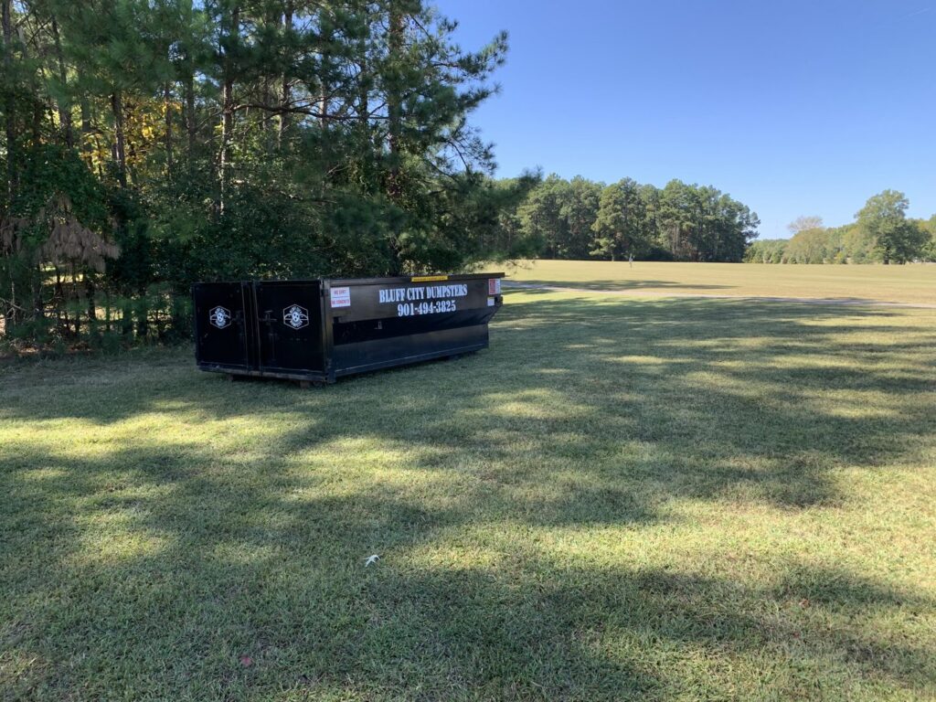 A Bluff City Dumpsters roll-off dumpster placed in a wide grassy field, ready for junk removal in Memphis, TN.
