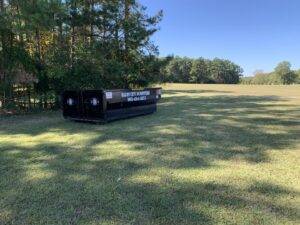 A Bluff City Dumpsters roll-off dumpster placed in a wide grassy field, ready for junk removal in Memphis, TN.