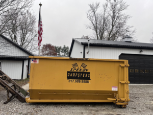 A Speedy Dumpsters roll-off container in a gravel area with an American flag in Brownsburg, IN.