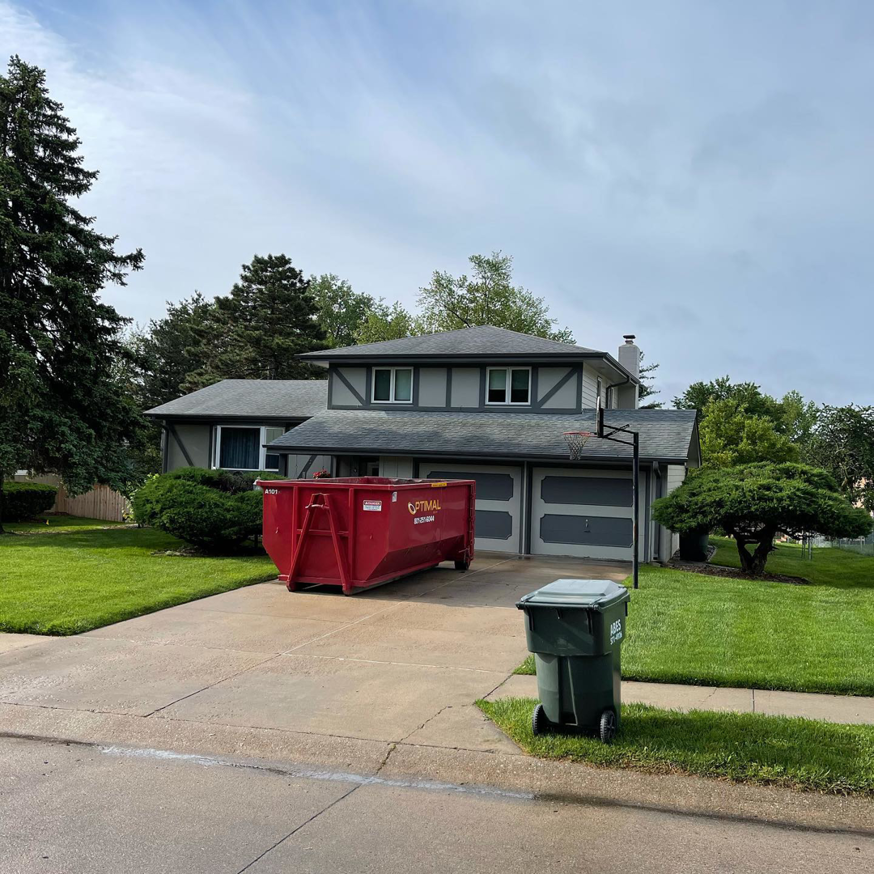 A red roll-off dumpster from Optimal Roll-Offs placed in a residential driveway in Papillion, NE.