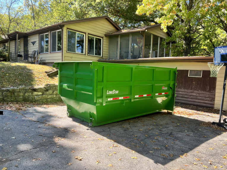 A green dumpster placed in a residential driveway for a junk removal project by Proper Dumpster Rentals in Kansas City, KS.