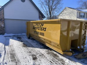 A Speedy Dumpsters roll-off container in a snowy residential driveway in front of a garage in Brownsburg, IN.