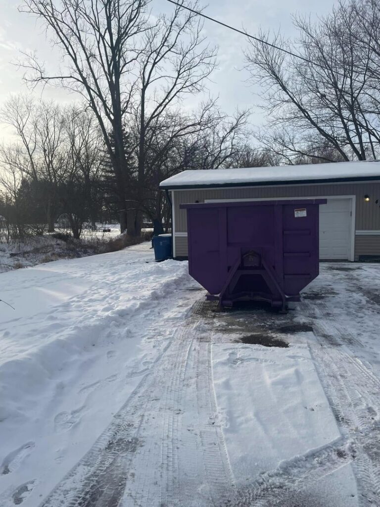 A DumpDog purple dumpster placed in a snowy residential driveway for winter junk removal in Flint, MI.