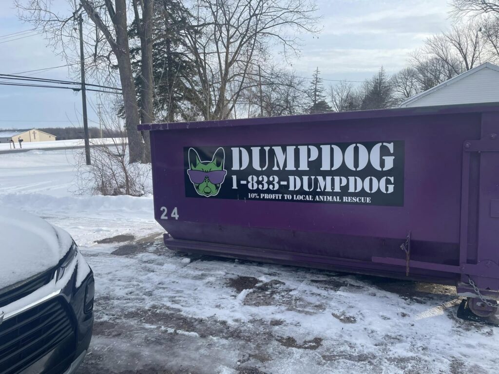 A DumpDog purple dumpster in a snowy residential driveway, ready for junk removal in Flint, MI.