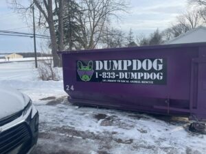 A DumpDog purple dumpster in a snowy residential driveway, ready for junk removal in Flint, MI.