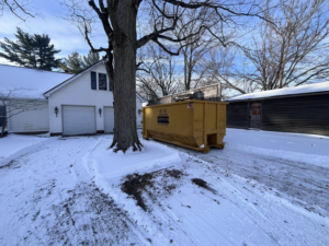 A Speedy Dumpsters roll-off container in a snowy residential driveway near a garage in Brownsburg, IN.