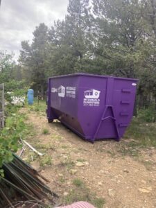 A McDonald Dumpsters purple dumpster placed in a wooded area for junk removal in Bar Nunn, WY.