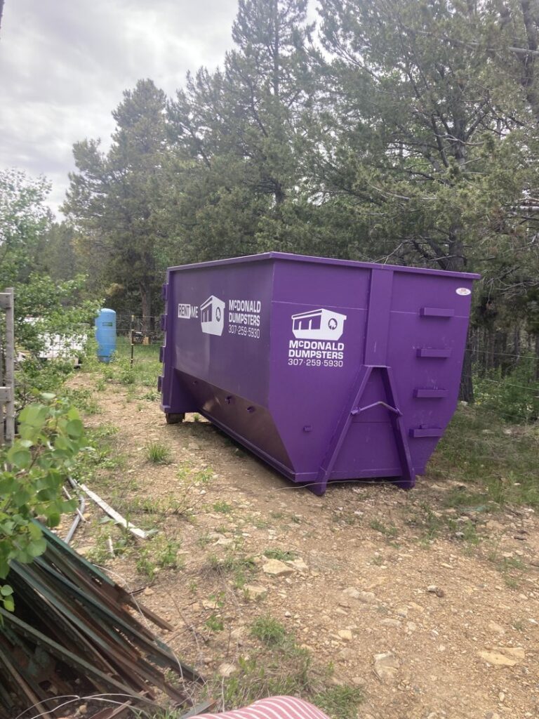 A McDonald Dumpsters purple dumpster placed in a wooded area for junk removal in Bar Nunn, WY.