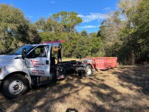A Vetcans Dumpster Rental truck with a red dumpster in a wooded area in Jacksonville, FL.