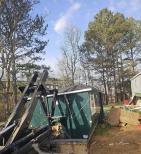 A green dumpster being loaded onto a truck, with another dumpster nearby, by Beetles Dumpsters Rental & Junk Removal in Huntsville, AL.