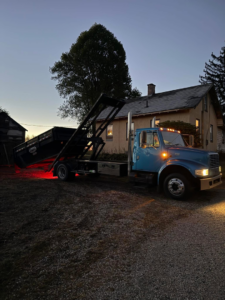 A blue roll-off truck loading or unloading a dumpster for junk removal services at dusk by Wagners Property Services LLC in Canton, OH.