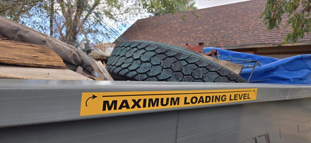 A close-up of a Trash Panda dumpster showing the 'Maximum Loading Level' sticker and a tire inside, in Carson City, NV.