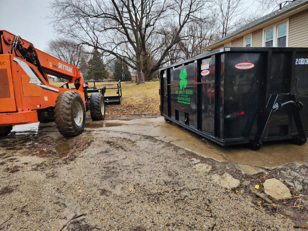 A KC Brothers Disposal dumpster parked next to a telehandler, indicating a construction or large cleanup project in Kansas City, MO.