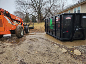A KC Brothers Disposal dumpster parked next to a telehandler, indicating a construction or large cleanup project in Kansas City, MO.