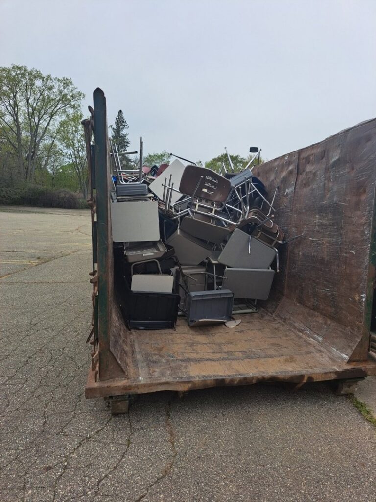 A large dumpster filled with office chairs and furniture for removal by Remove Recycle Remarket in Troy, MI.