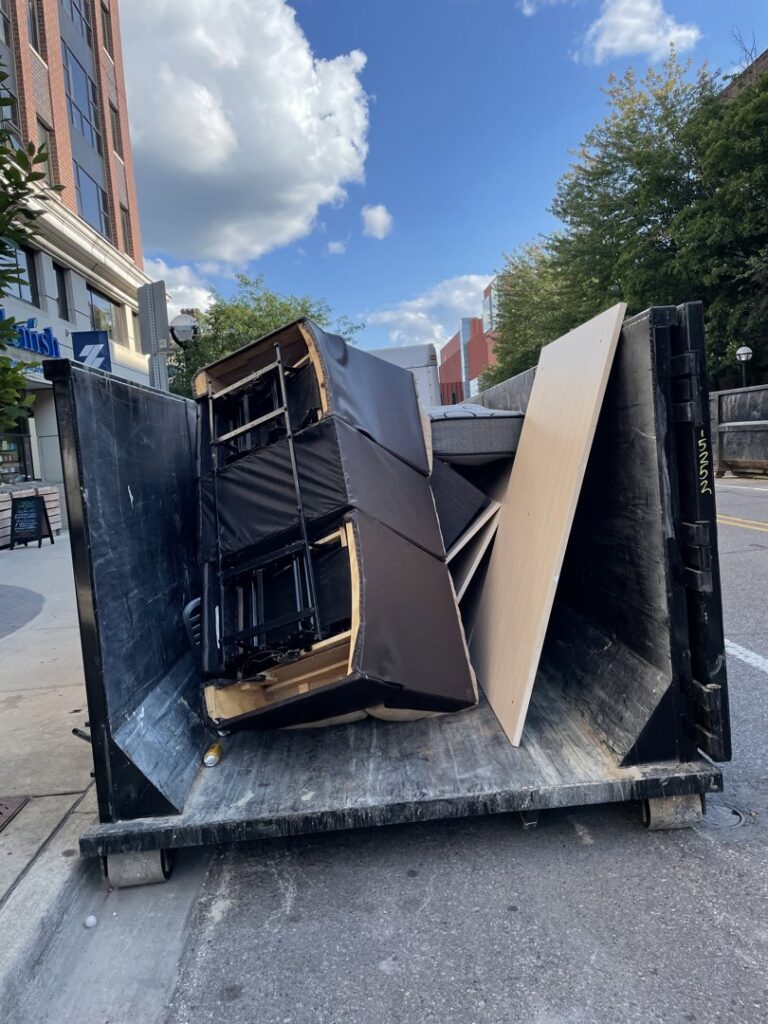 A large dumpster filled with old furniture and wood panels, showcasing a junk removal service by Prestige Junk Removal & Hauling in Detroit, MI