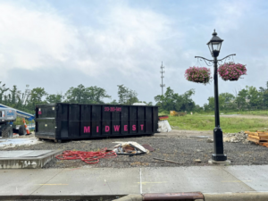 A Midwest Containers dumpster on a gravel construction site with red hoses and debris, ready for junk removal in Cincinnati, OH.