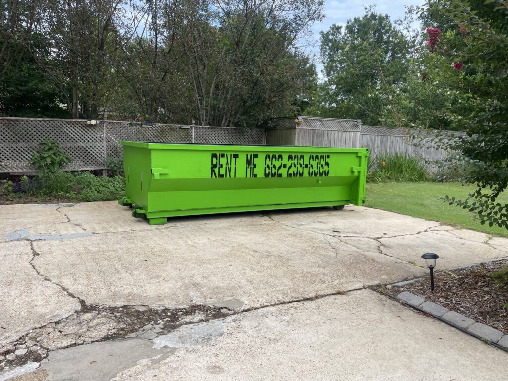 A bright green dumpster placed on a residential driveway for junk removal by Tristate Dumpsters LLC in Greenville, MS.