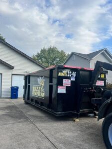 A Buzz Dumpster & Junk Removal truck preparing to pick up a dumpster from a residential driveway in Troy, MO.