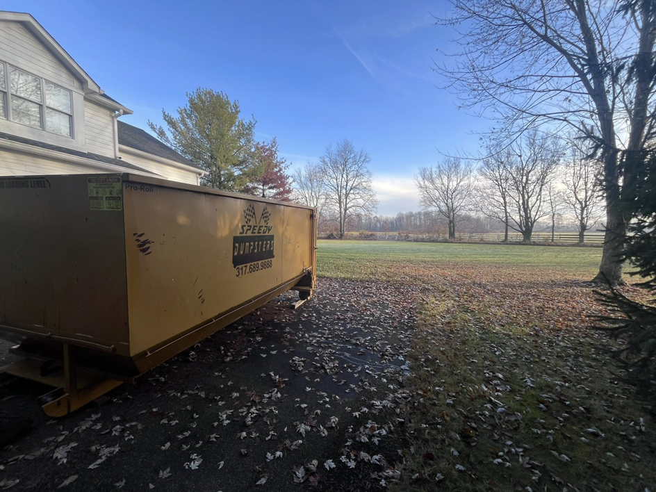 A Speedy Dumpsters roll-off container on a driveway with fallen leaves in Brownsburg, IN.
