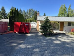 A red dumpster from Cascade Container and Recycling placed on a gravel driveway next to a house in Seattle, WA.