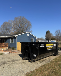 A branded dumpster from Disposal Pro Haul Away Services on a gravel driveway next to a residential home in Charlotte, NC.