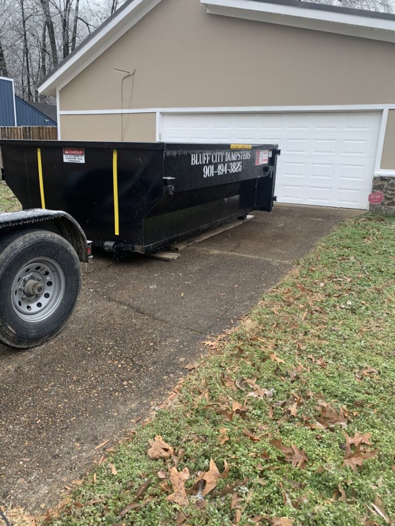 A Bluff City Dumpsters roll-off dumpster placed on a residential driveway next to a garage in Memphis, TN.