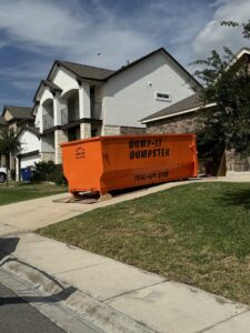 An orange Dump-IT Dumpster Rentals LLC dumpster placed on a residential driveway in Laredo, TX, ready for junk removal.