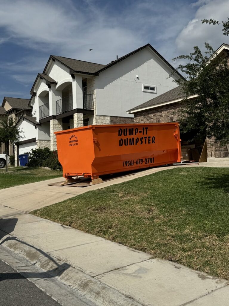 An orange Dump-IT Dumpster Rentals LLC dumpster placed on a residential driveway in Laredo, TX, ready for junk removal.