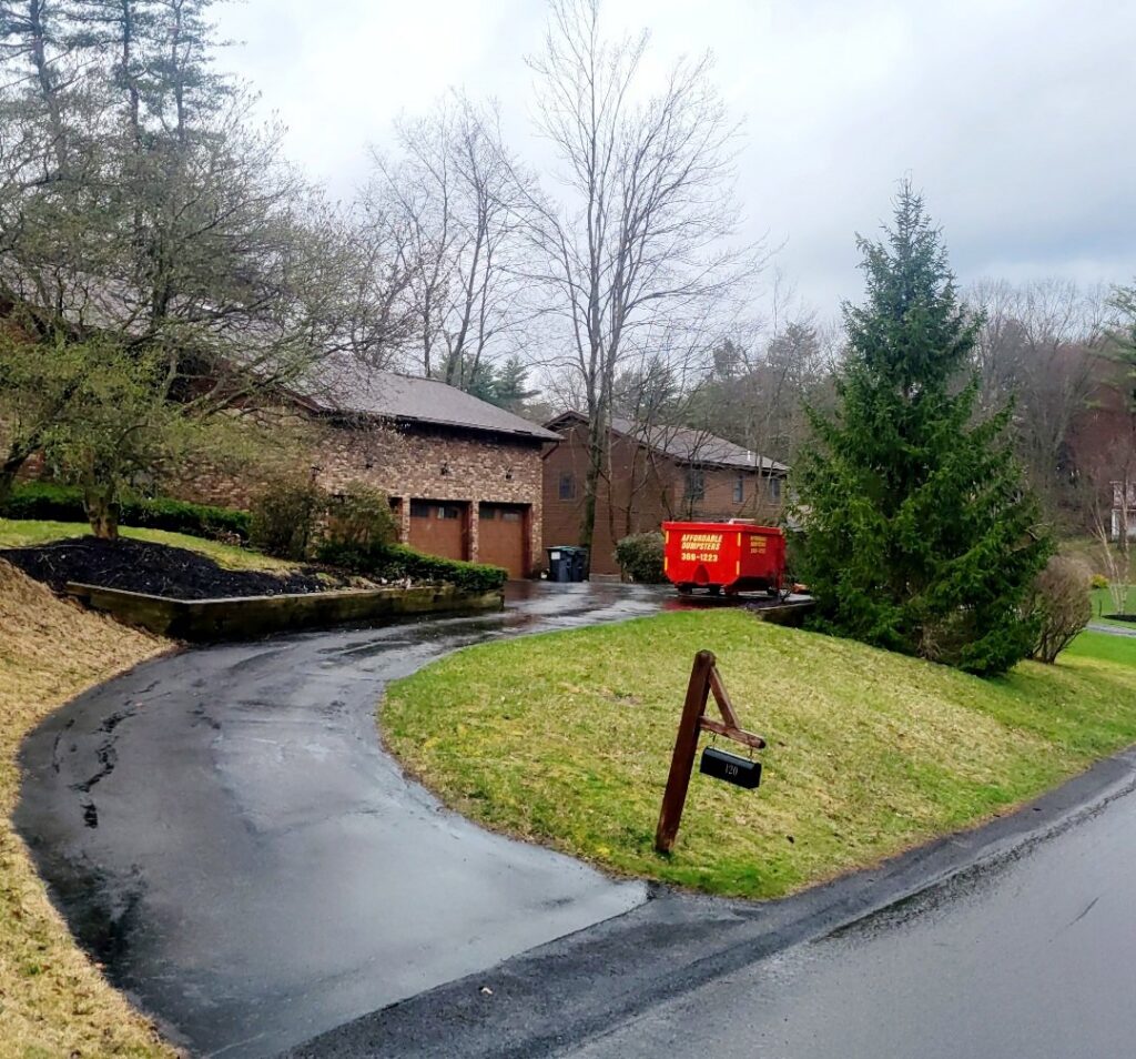 A red dumpster from Affordable Dumpsters positioned on a sloped residential driveway in Watervliet, NY.