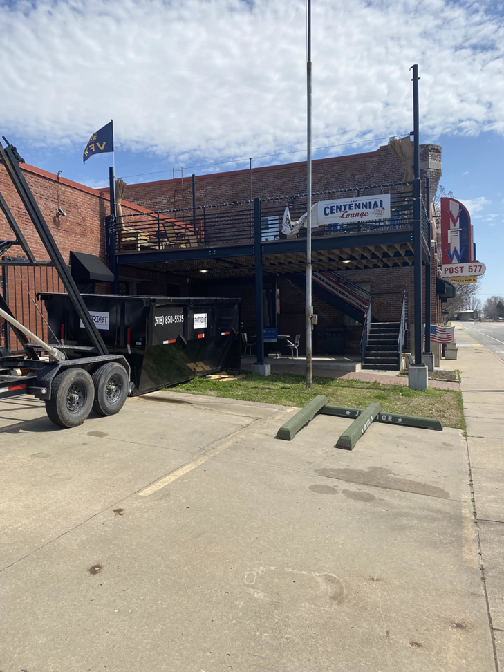 A black dumpster on a trailer parked in front of a commercial building by Patriot Dumpster Rental and Hauling in Tulsa, OK.