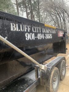 A Bluff City Dumpsters roll-off dumpster on a trailer next to another storage container in Memphis, TN.