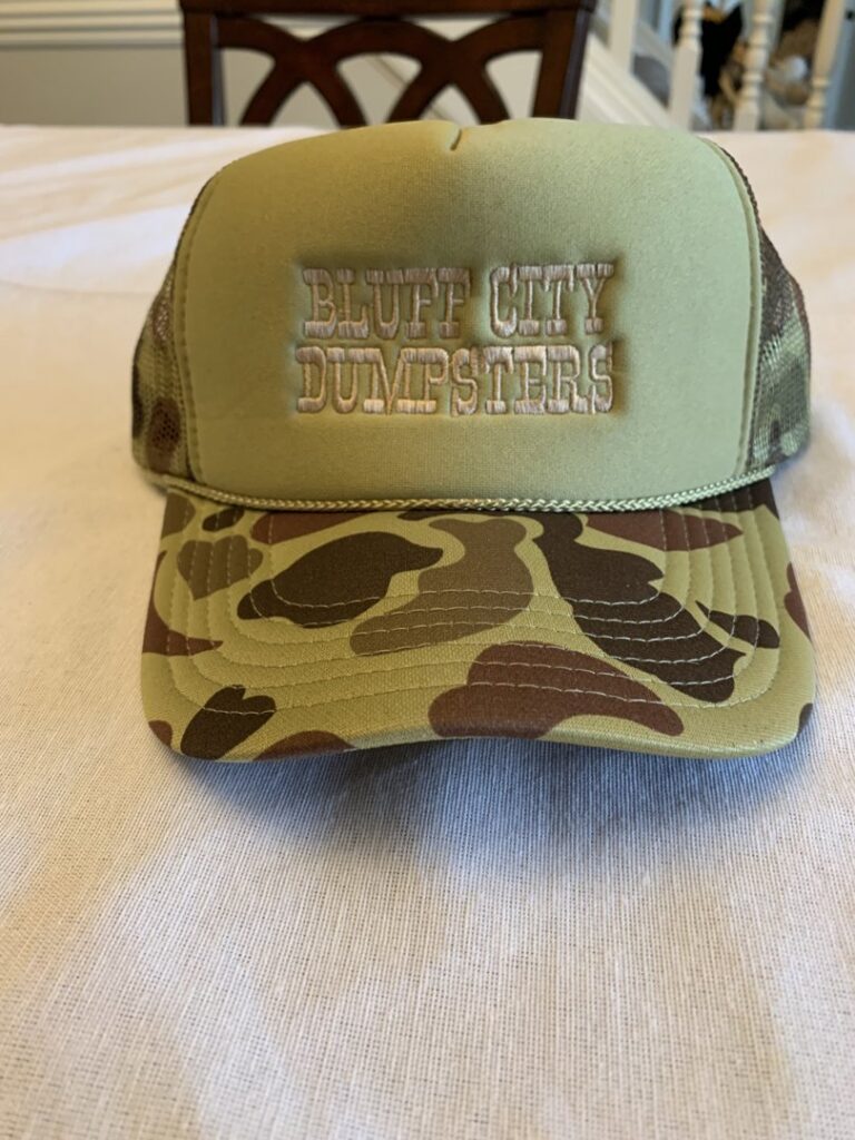 A Bluff City Dumpsters roll-off dumpster on a trailer in a wooded area, ready for debris collection in Memphis, TN.