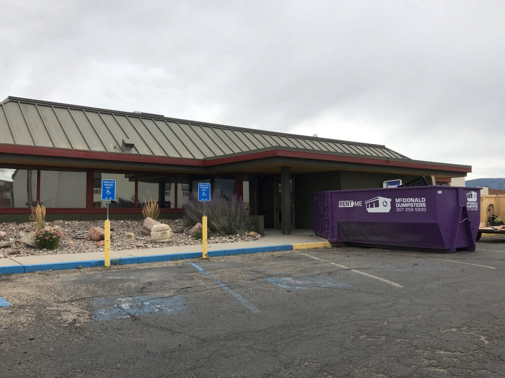A McDonald Dumpsters purple dumpster placed outside a commercial building in Bar Nunn, WY.
