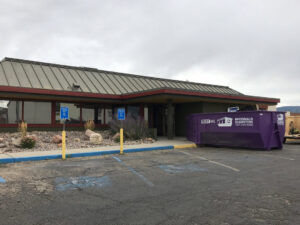 A McDonald Dumpsters purple dumpster placed outside a commercial building in Bar Nunn, WY.